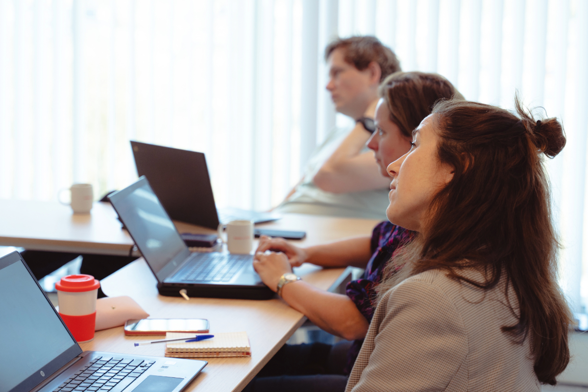 Teamleden overleggen bij een bord en laptop – symbool voor het kritisch herontwerpen van teamoverleggen in het onderwijs