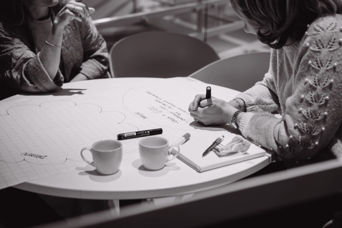 Handen van teamleden aan een tafel met stiften en papier – visuele metafoor voor samen leren en teamontwikkeling in het onderwijs